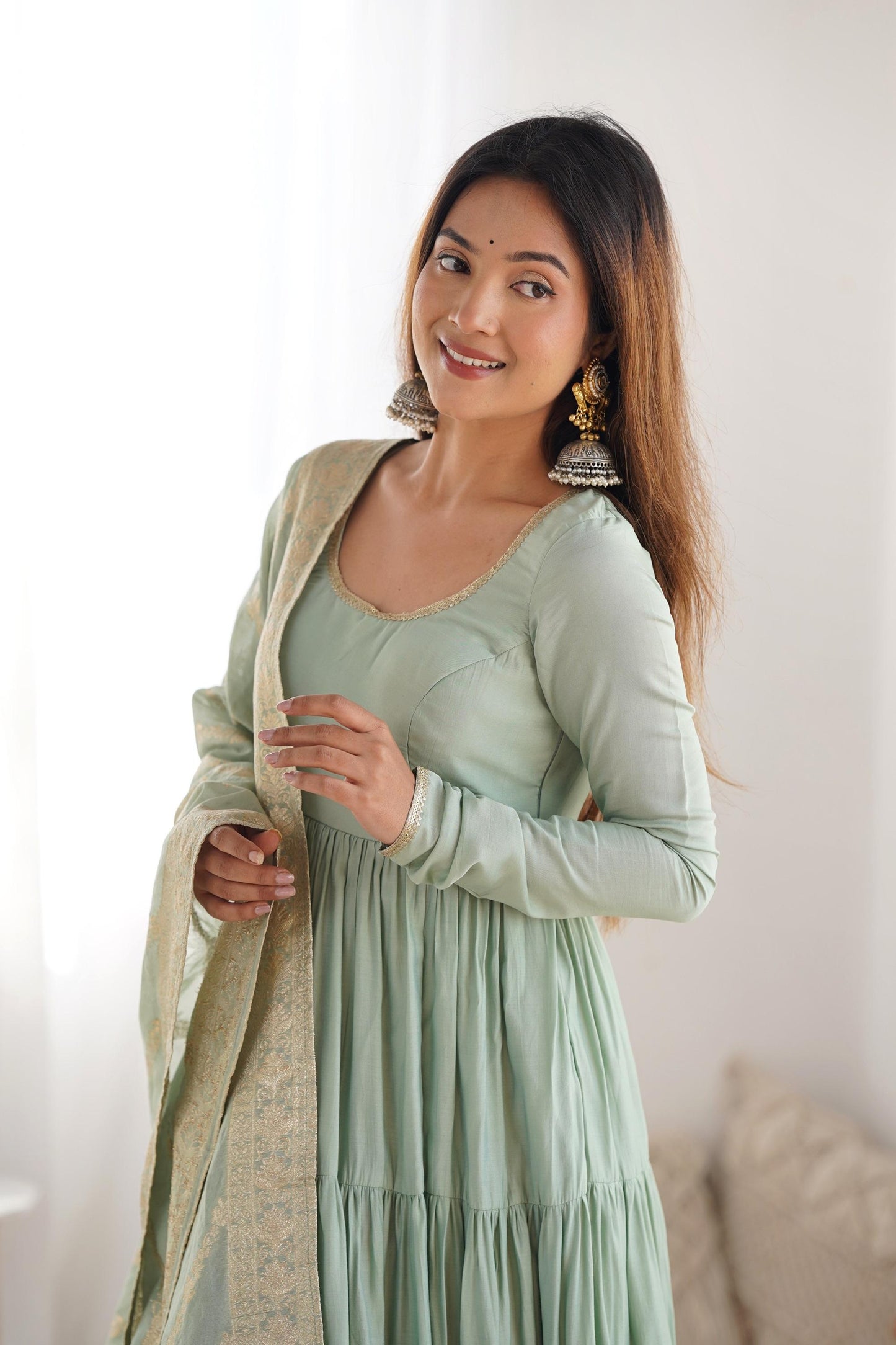 A woman wearing a flowing light green Anarkali suit with a heavy zari woven dupatta