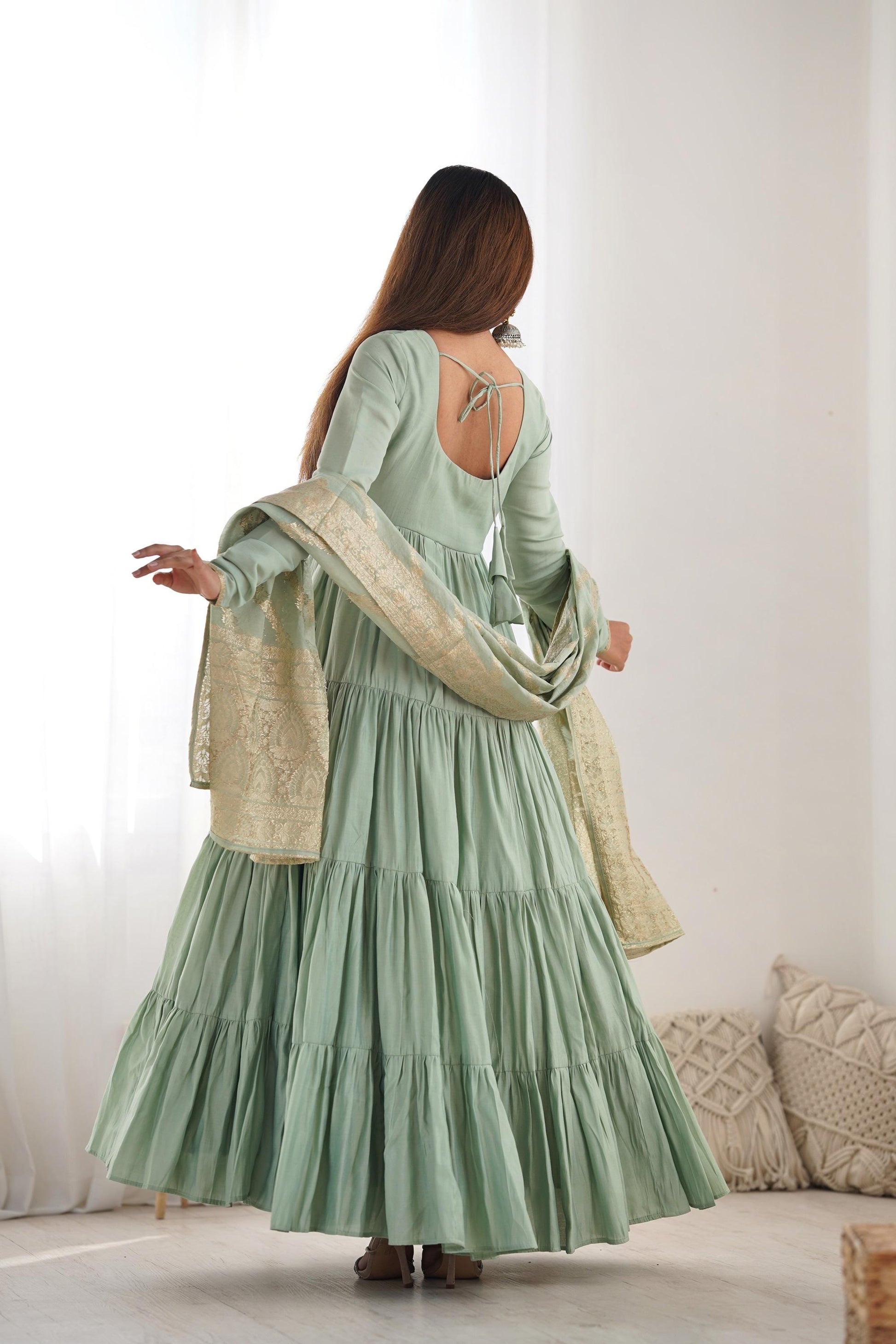 A woman wearing a flowing light green Anarkali suit with a heavy zari woven dupatta