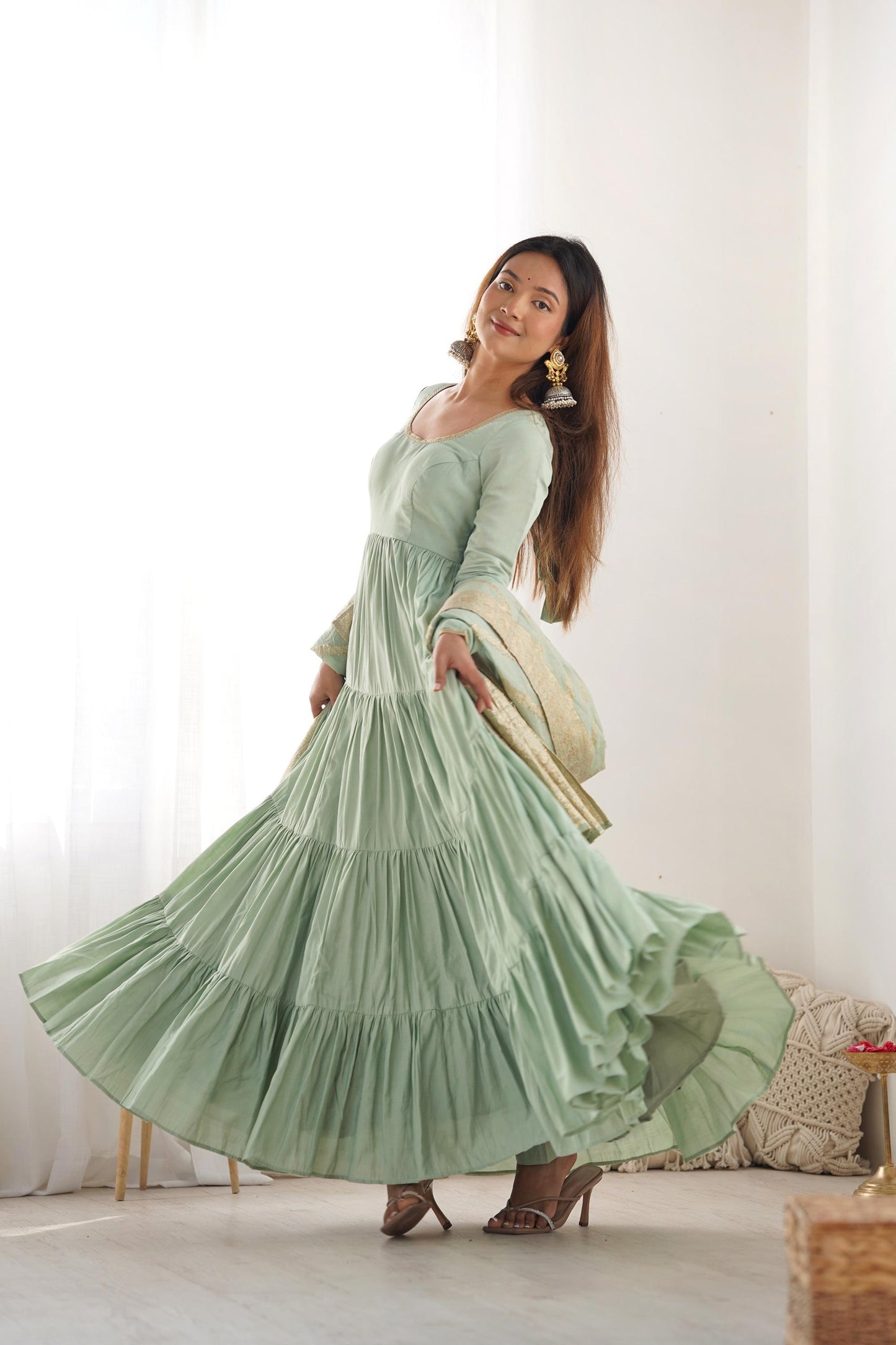 A woman wearing a flowing light green Anarkali suit with a heavy zari woven dupatta
