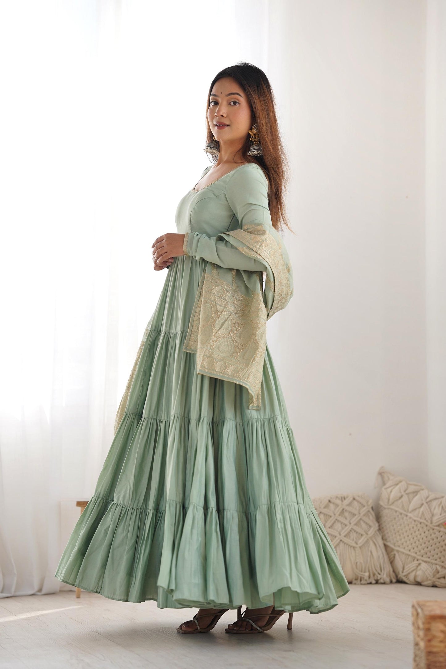 A woman wearing a flowing light green Anarkali suit with a heavy zari woven dupatta