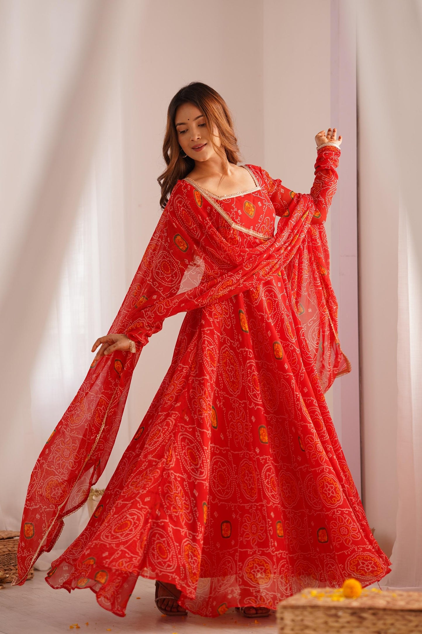A woman gracefully walking in a flowing red Anarkali suit set with a dupatta and bandhej print