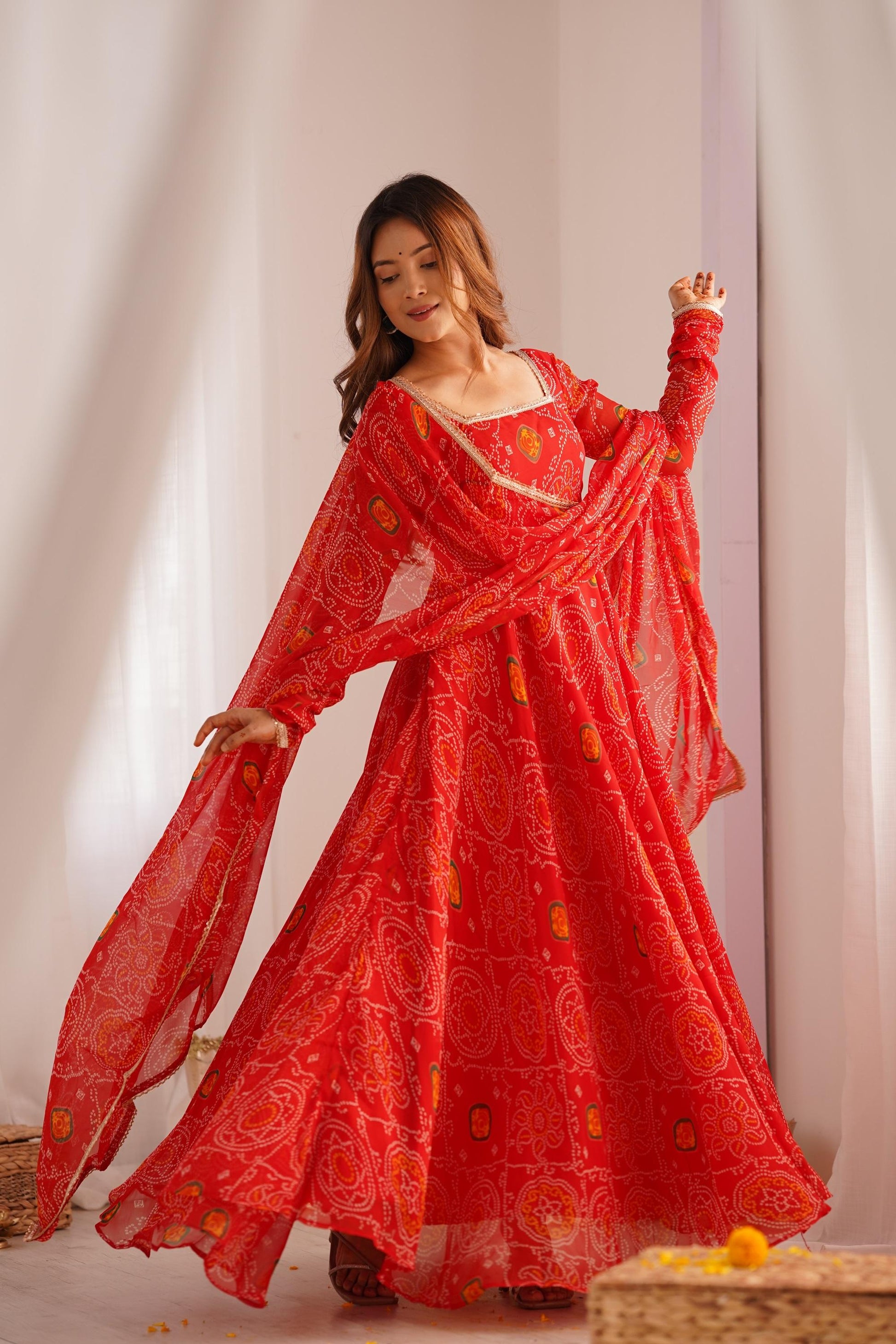 A woman gracefully walking in a flowing red Anarkali suit set with a dupatta and bandhej print