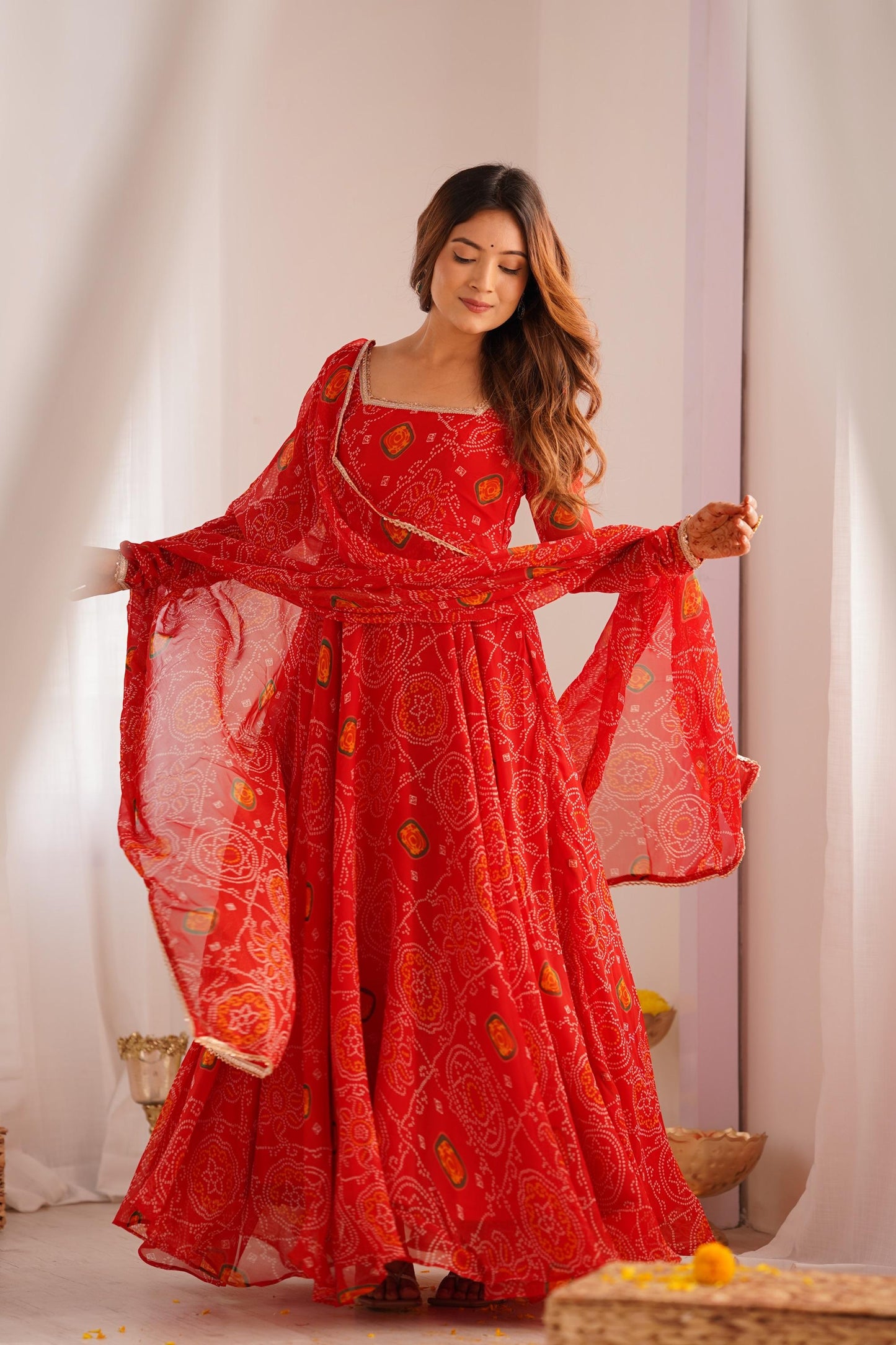 Three-quarter view of a woman wearing a flowing red Anarkali suit set with a dupatta, showcasing the overall look and the bandhej print